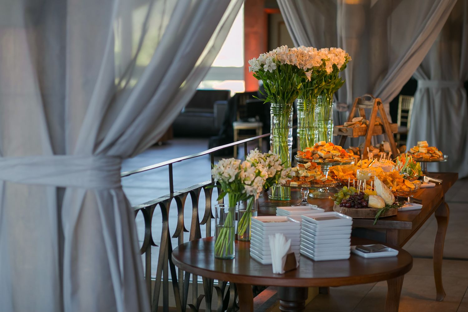 Wedding reception table setup with floral arrangements and elegant drapes in soft natural lighting.