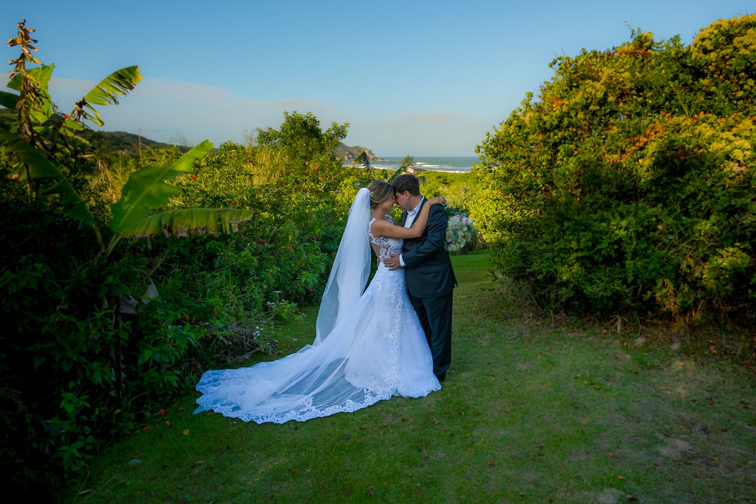 Scenic wedding portrait of couple on coastal path surrounded by lush greenery.