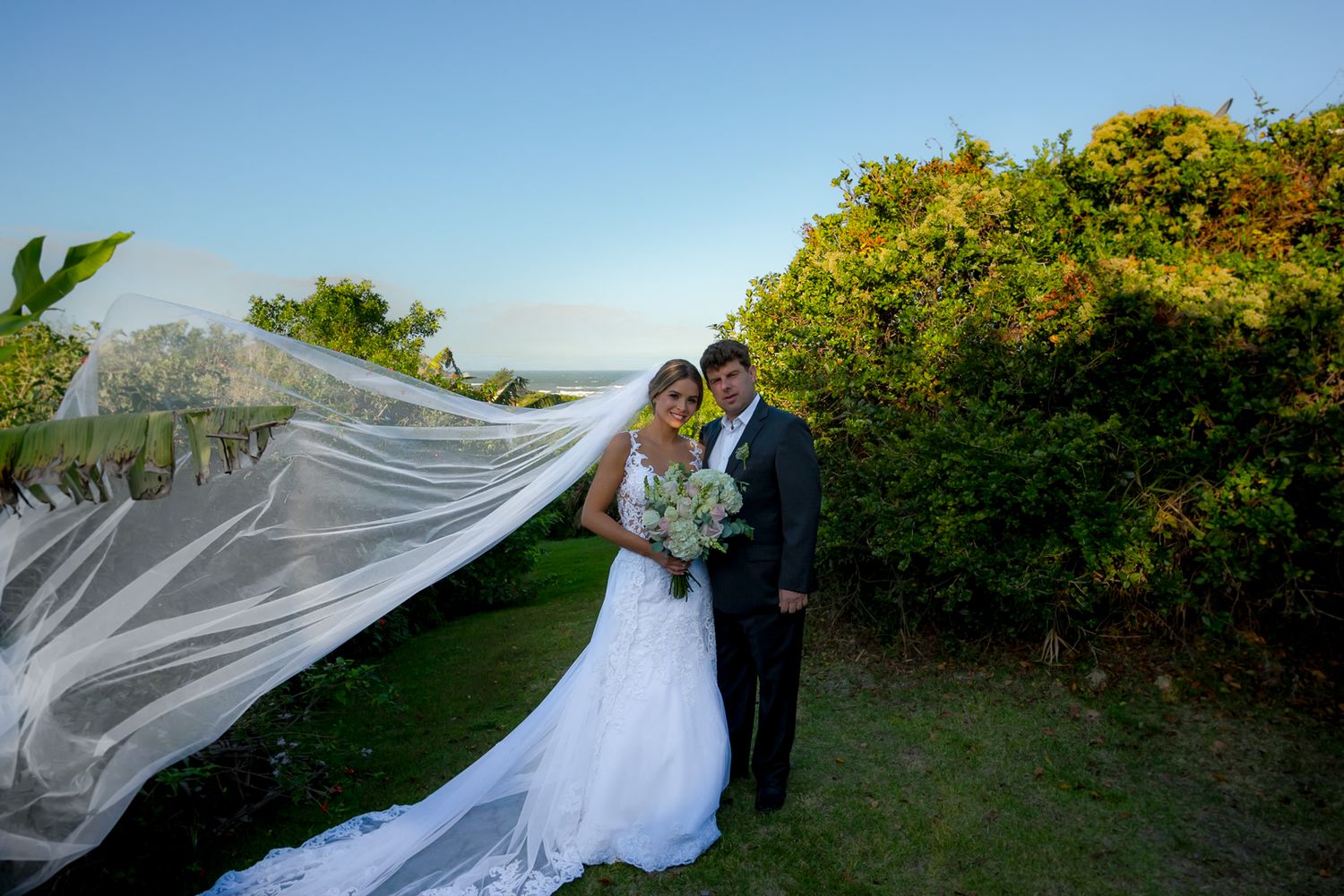 Dramatic veil shot of wedding couple against coastal landscape.