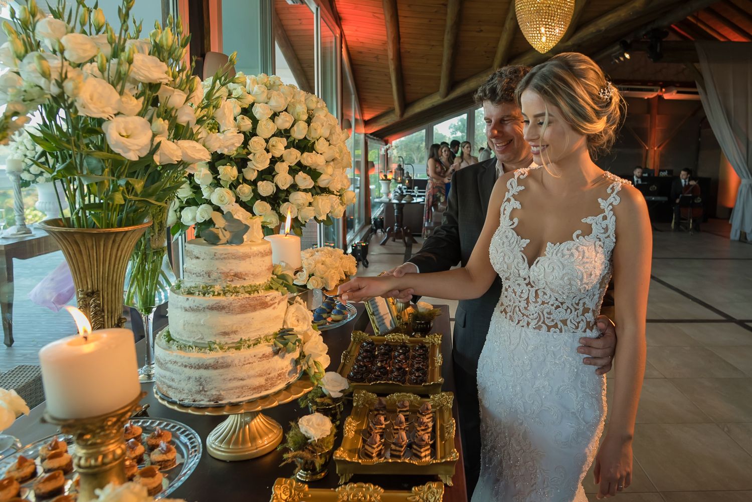 An elegant white wedding cake display with fresh flowers and dessert table at a reception.