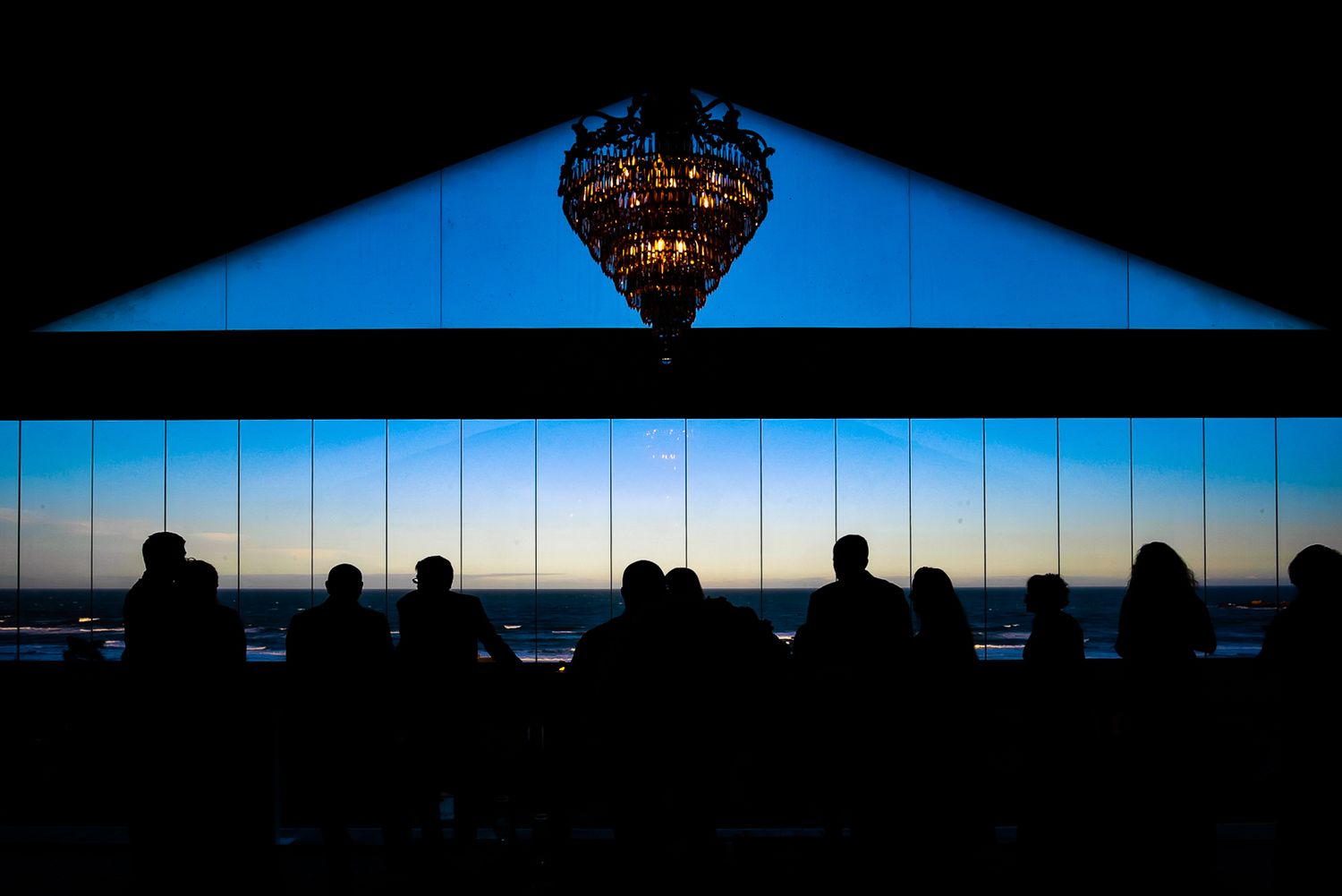 Silhouettes of guests against large windows with a dramatic sunset and ornate chandelier.