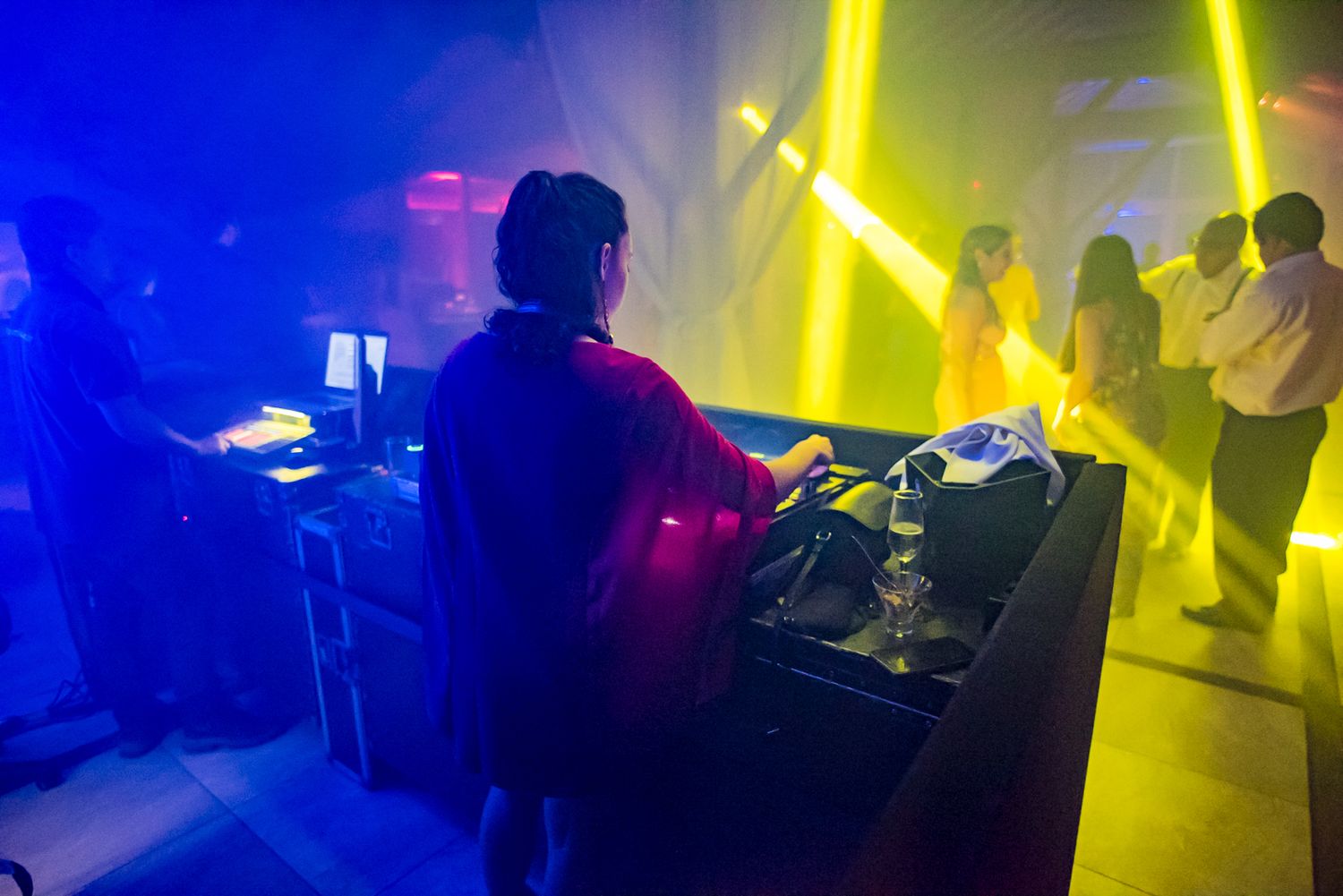 A DJ mixing music at a party with colorful yellow and blue lighting effects.