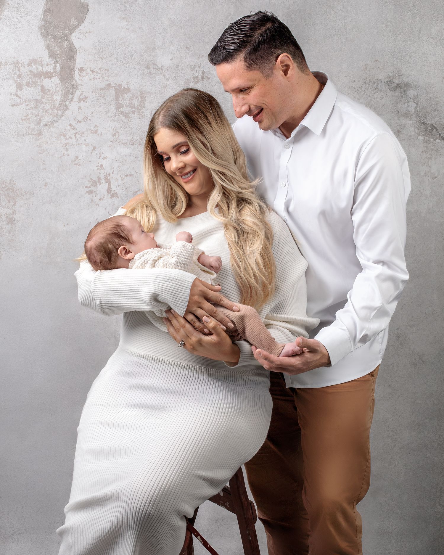 Newborn family portrait, mother holding newborn lovingly the babies father gazing with love on newborn.