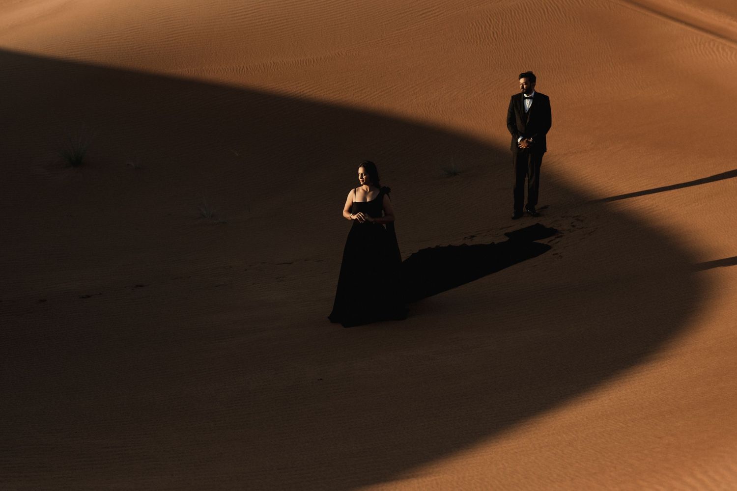 Dramatic aerial view of two figures casting long shadows on an orange-lit surface.