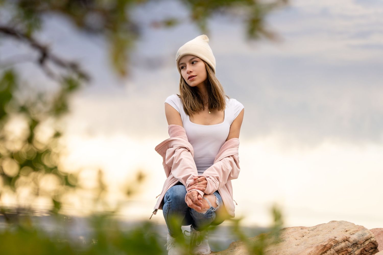 Someone in casual wear sitting on rocks during sunset wearing a beanie hat.
