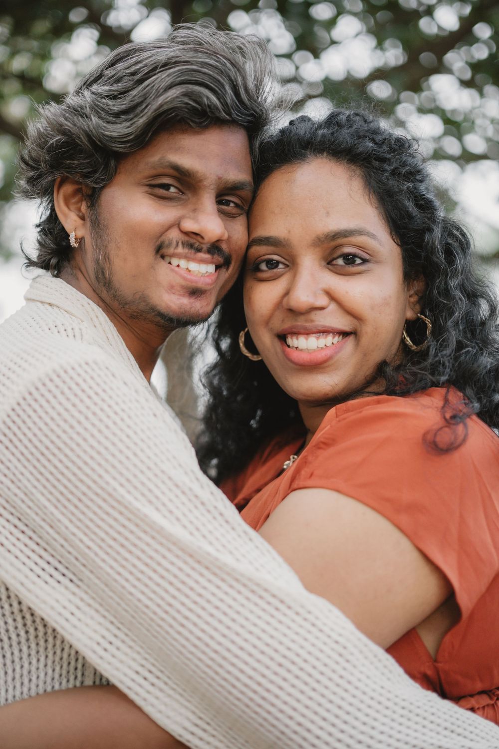 A couple smiles brightly while embracing outdoors with bokeh lighting effects.