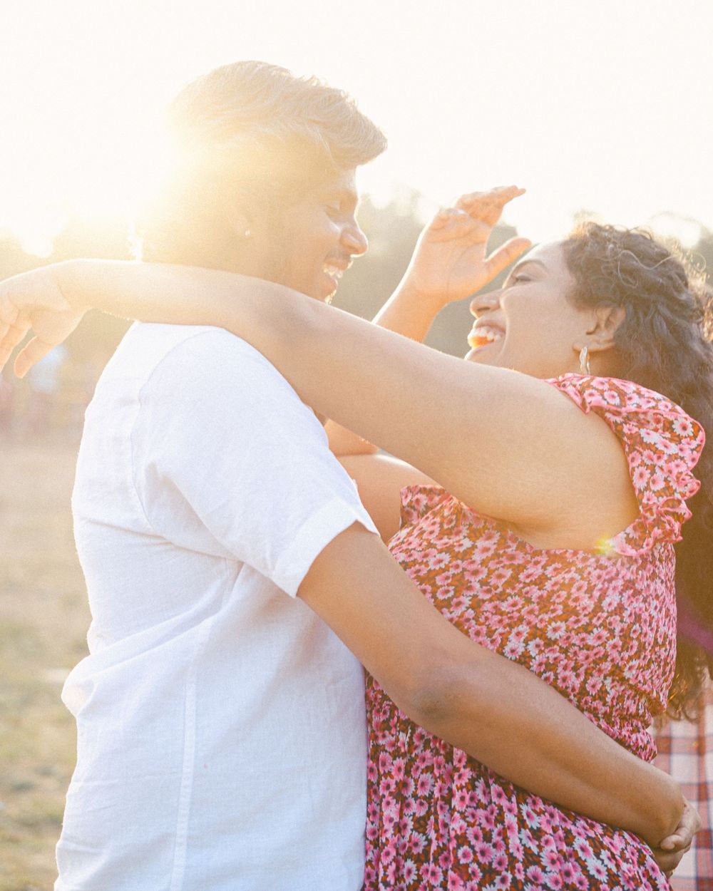 A couple shares a romantic embrace during golden hour with sunlight creating a warm glow.