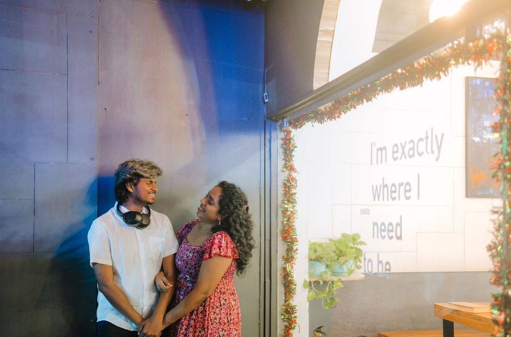 A romantic moment between a couple laughing against a blue wall with decorative lighting.