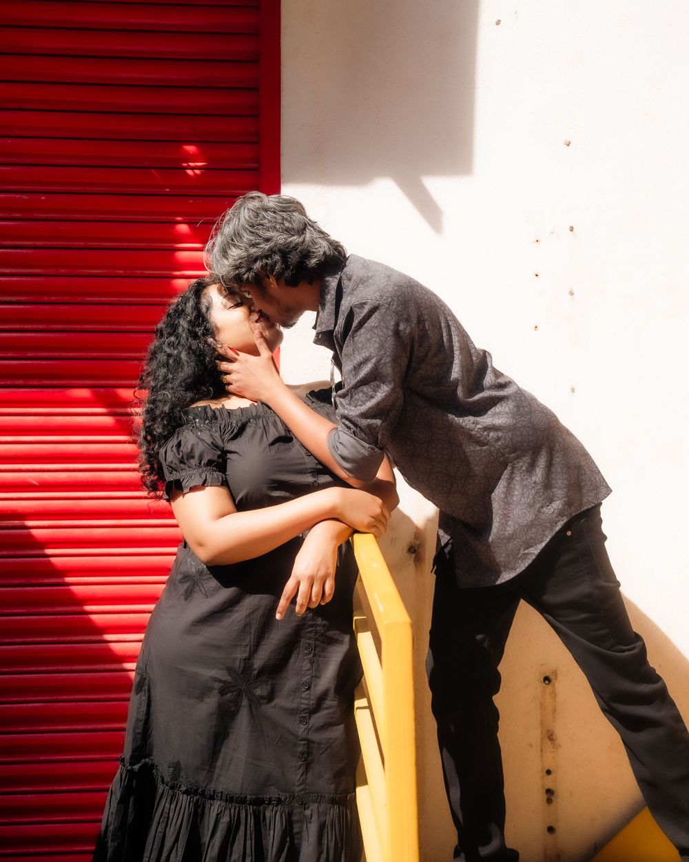 A romantic couple sharing an intimate moment against a red door with dramatic lighting.