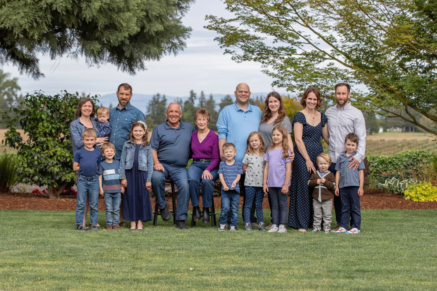 Family group embraces in a garden setting wearing coordinated white and pastel outfits.