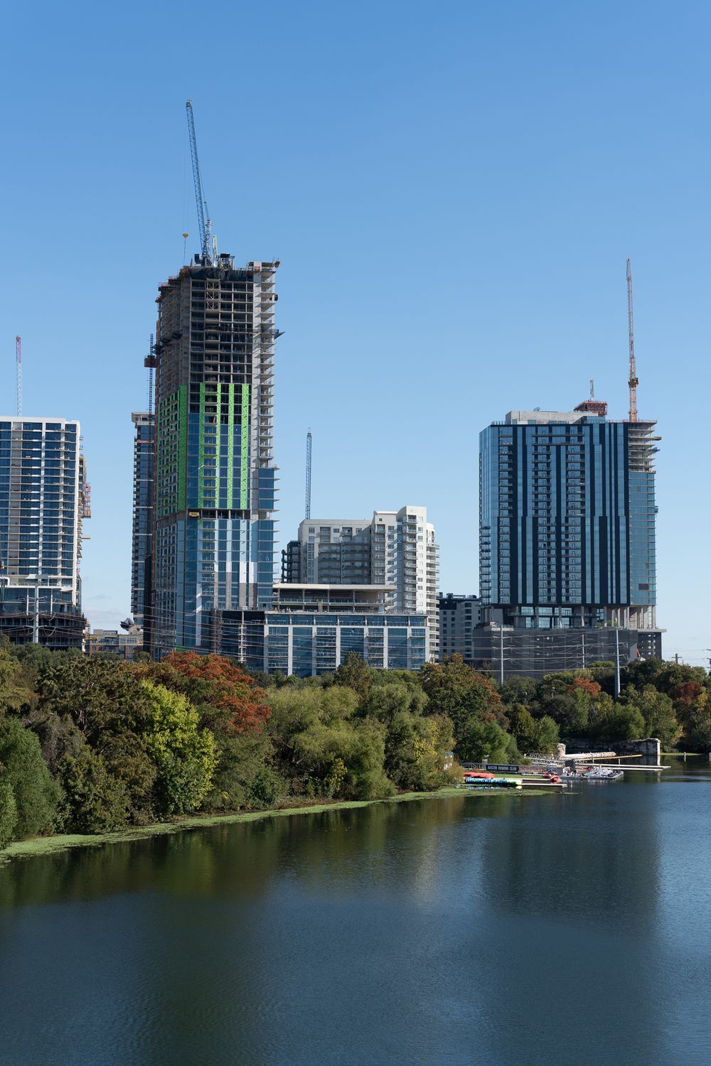 Construction of high-rise buildings along Austin's waterfront with cranes visible against blue sky.