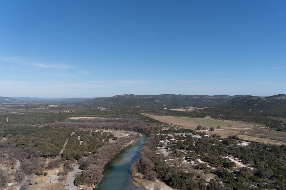 Aerial view of a winding river cutting through rolling hills and rural landscape on a sunny day.