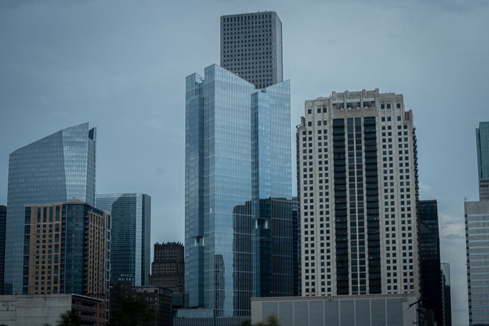 Modern glass skyscrapers and office buildings in an urban downtown area against an overcast sky.