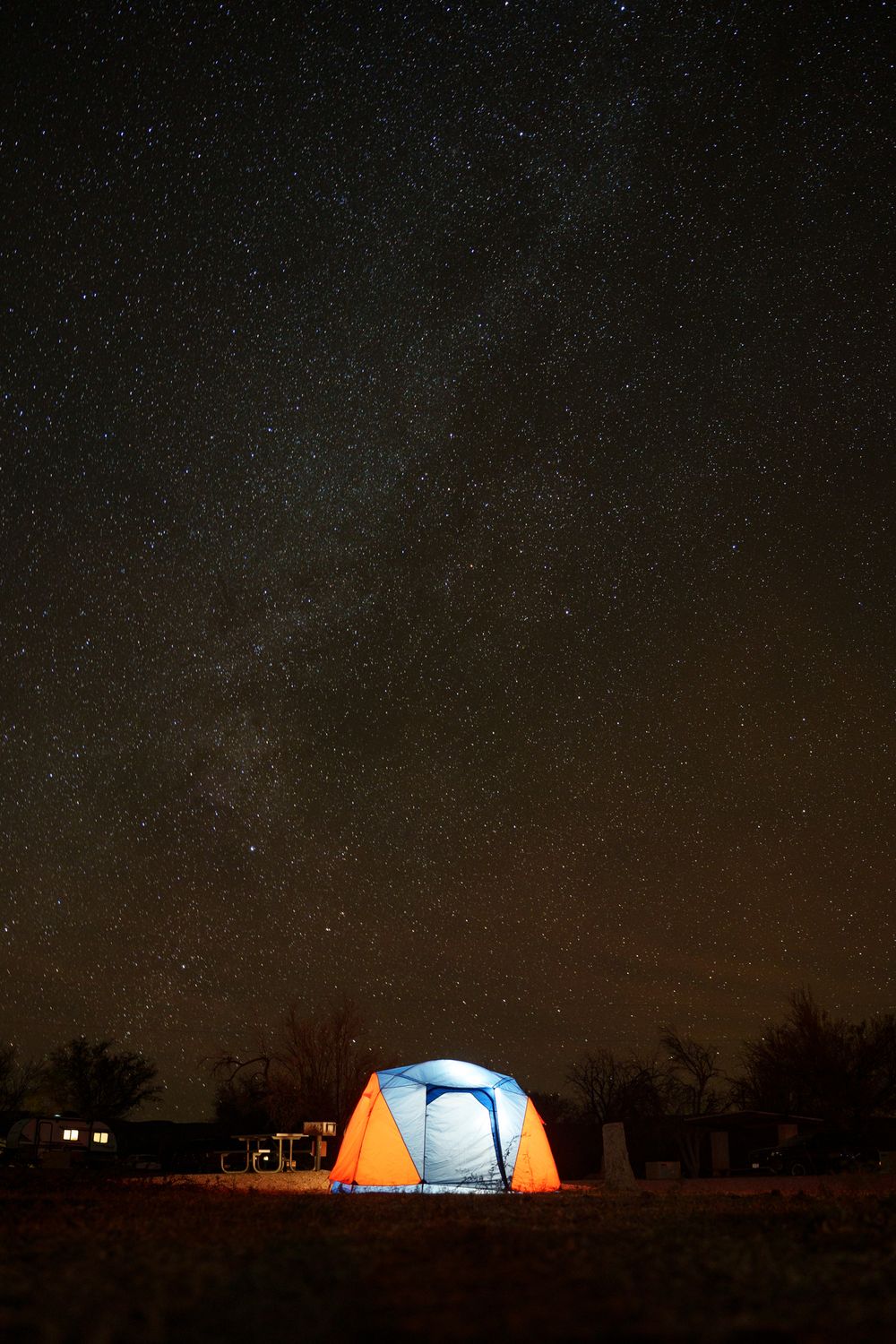 Illuminated camping tents glow against a dark starry night sky in a remote wilderness setting.