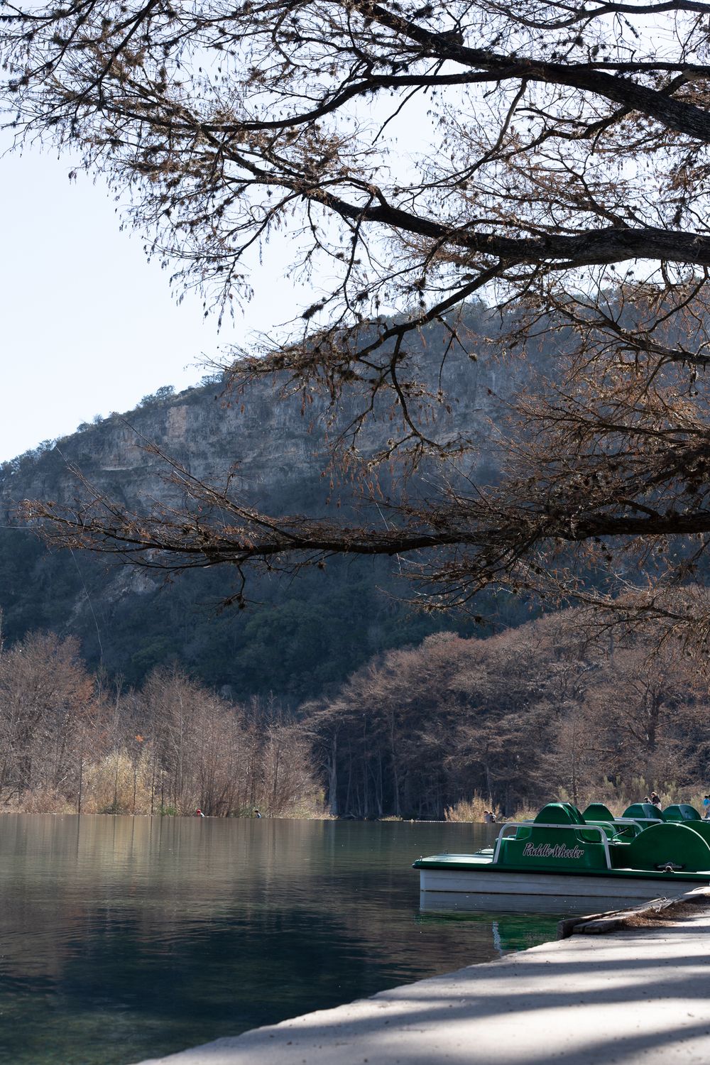 Paddle boats docked on a serene lake with winter trees and mountain backdrop.