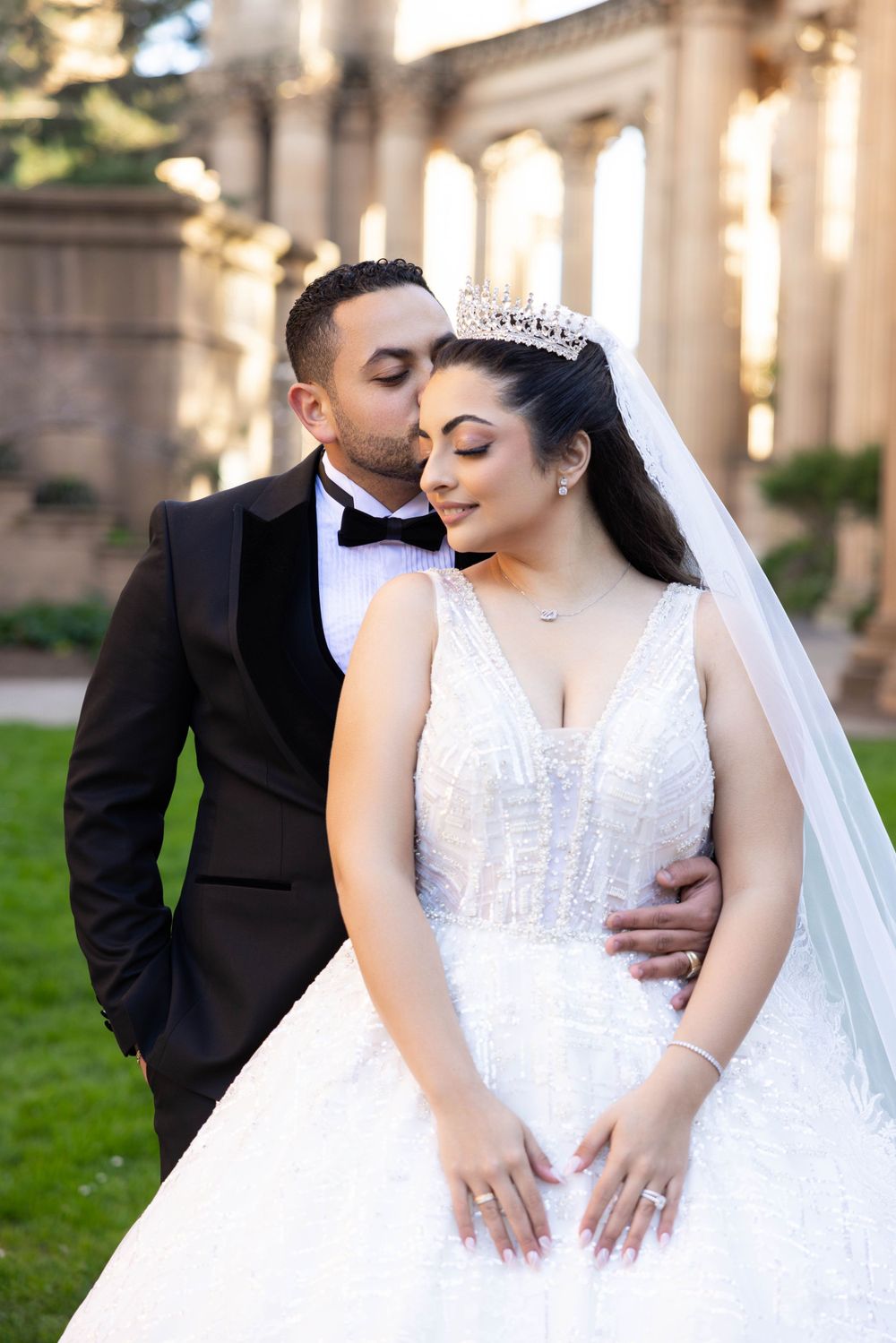 A romantic wedding portrait shows a couple in formal attire against a grand architectural backdrop.