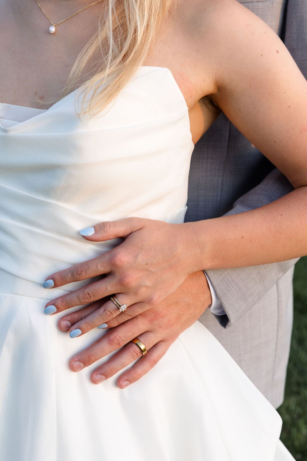 Close-up detail of a wedding ring on a hand resting against a white dress.