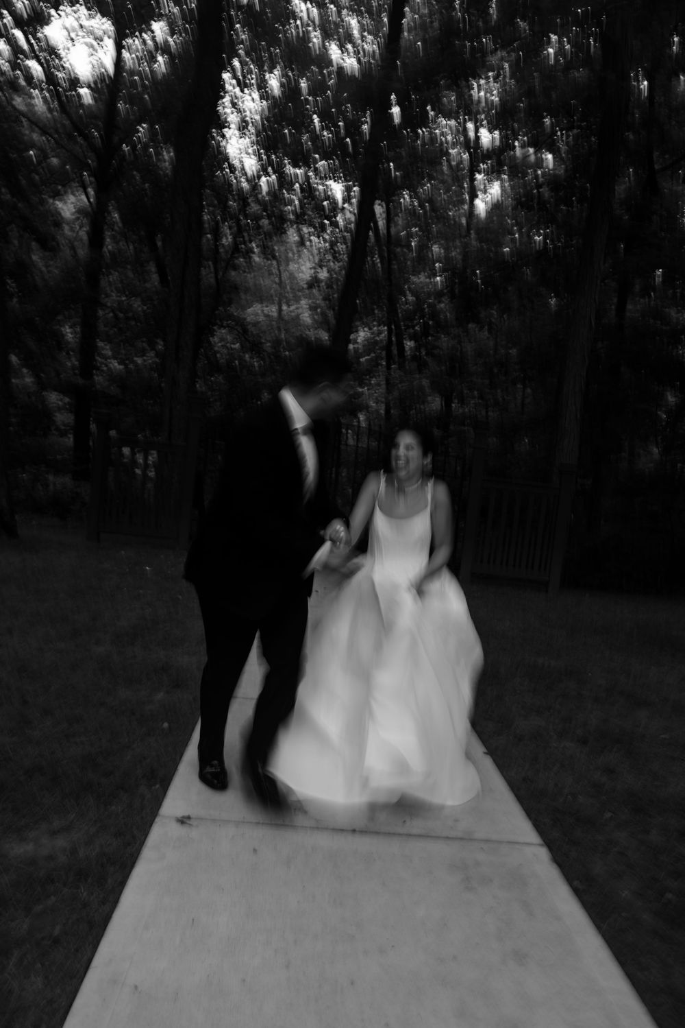 Black and white artistic wedding photograph showing dancing silhouettes on a light-colored platform outdoors.