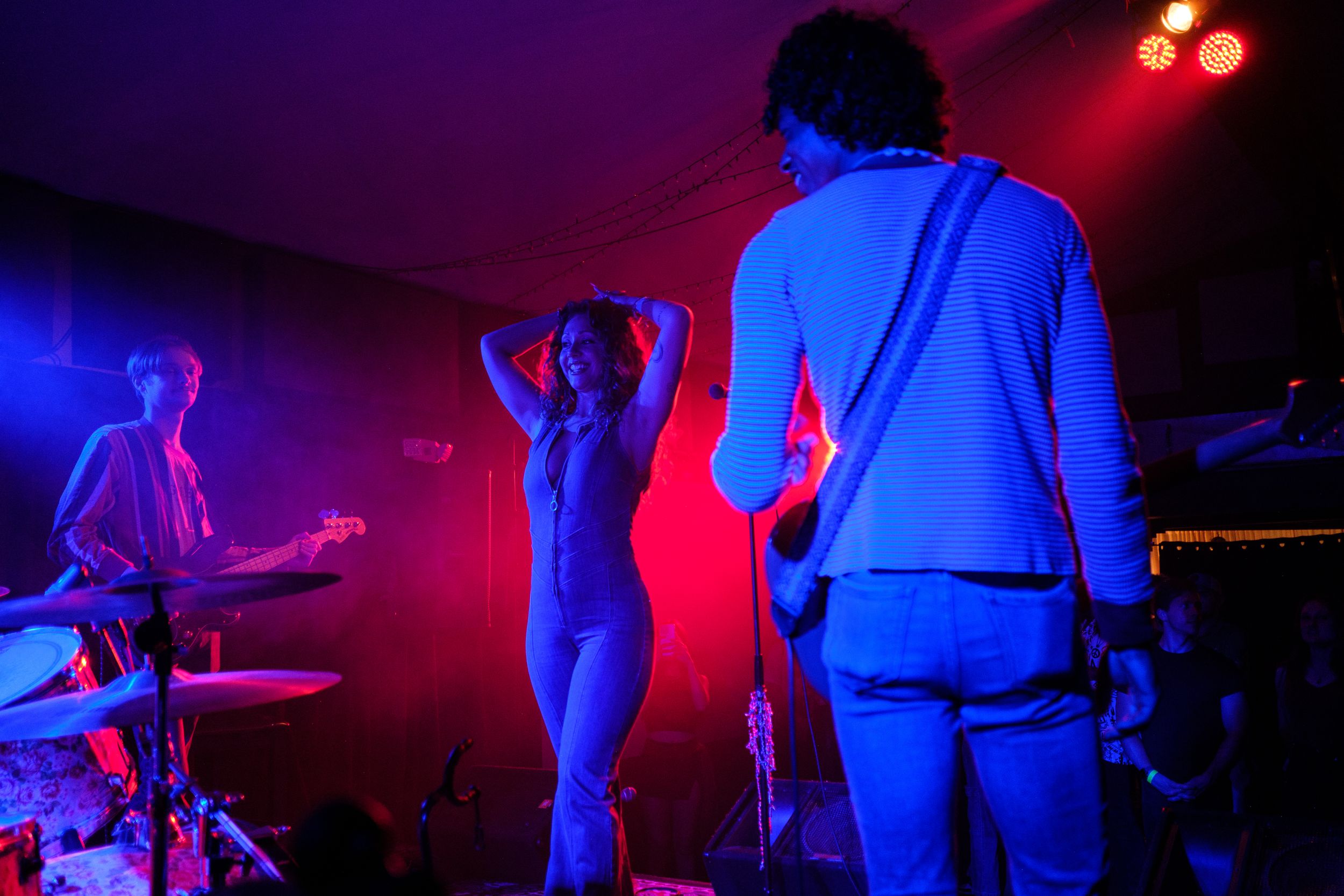 Musicians perform under dramatic red stage lighting creating silhouettes against a dark background.