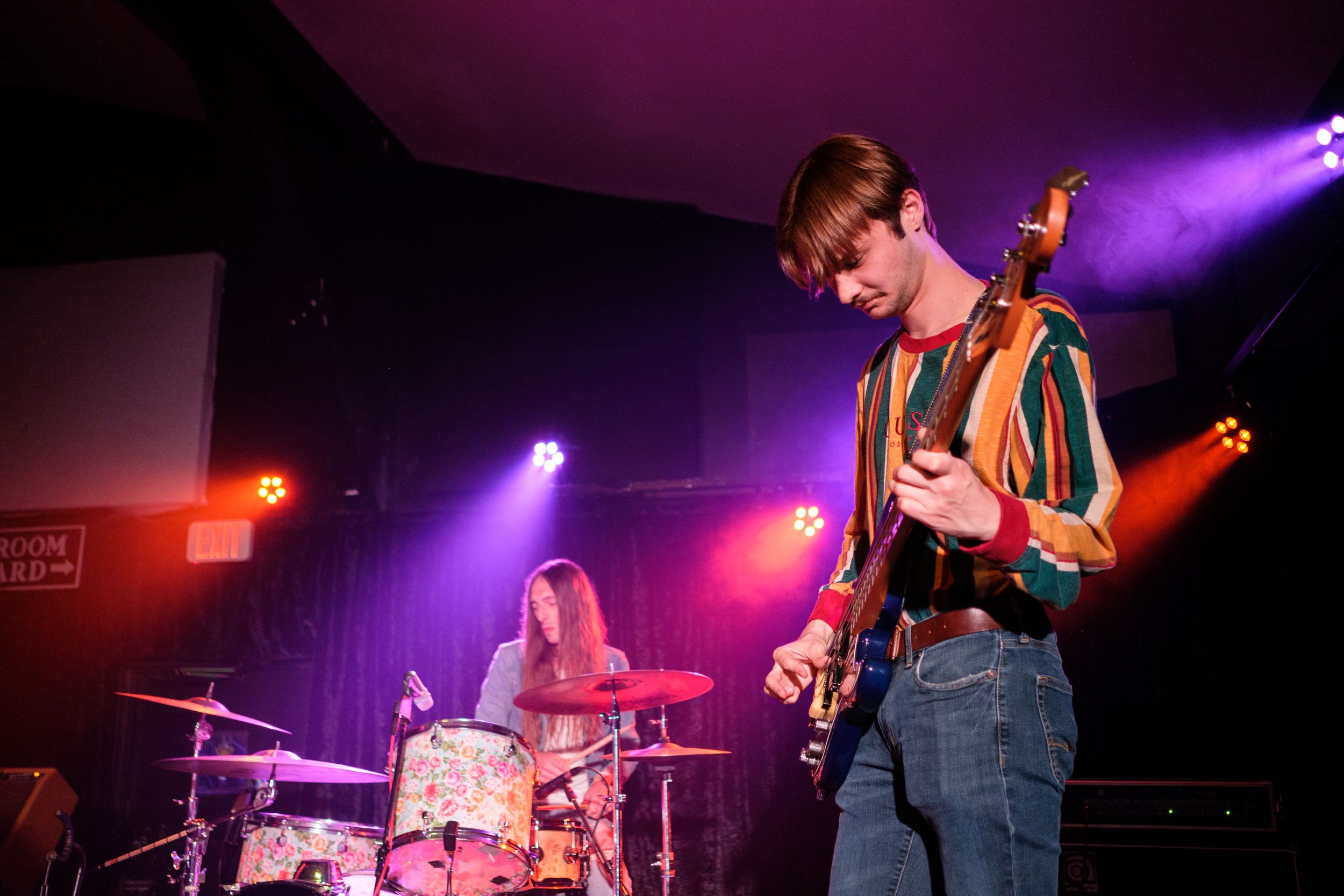 Musicians perform on stage with vibrant purple lighting and atmospheric effects.