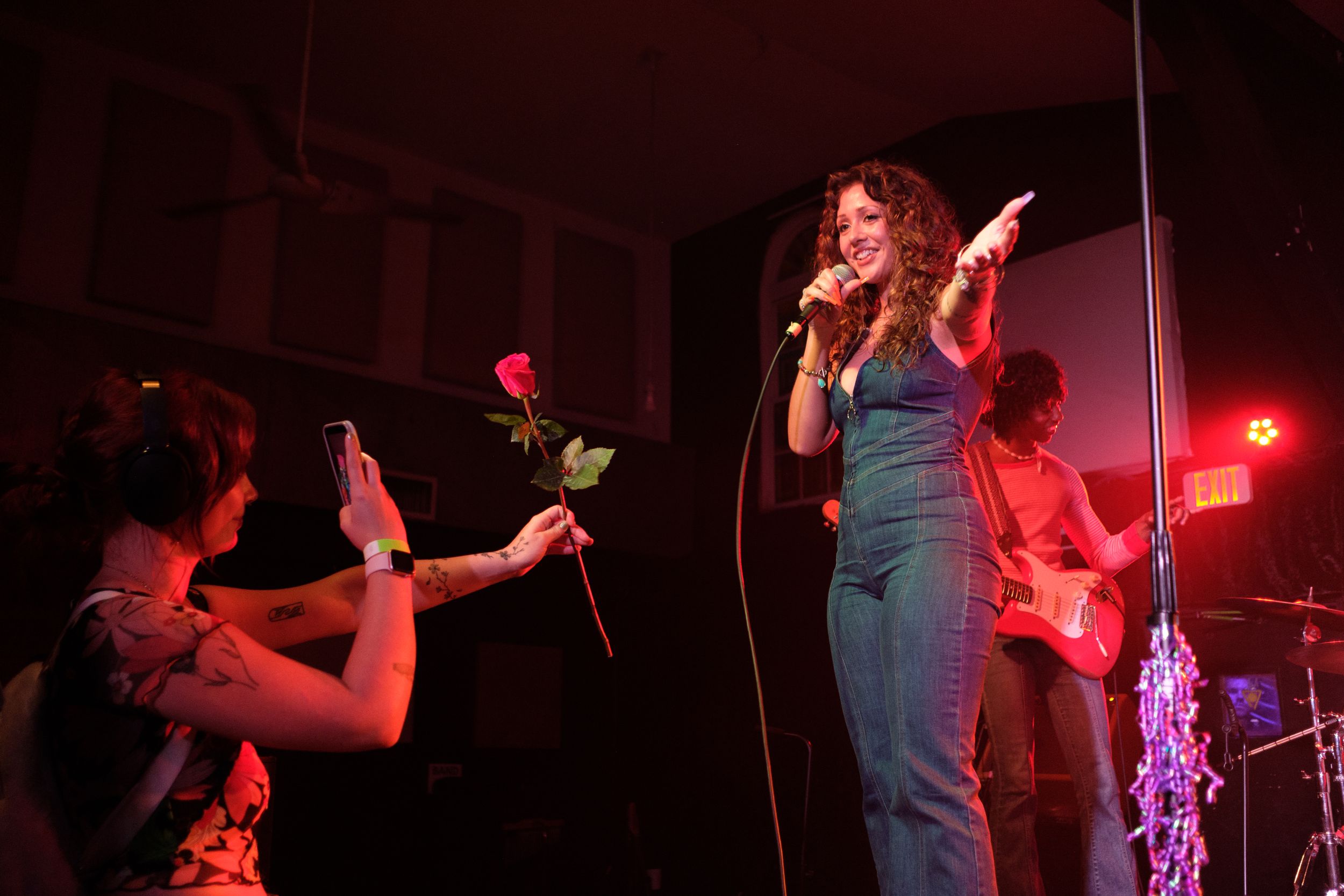 A performance on stage with red lighting shows band members and decorative string lights.