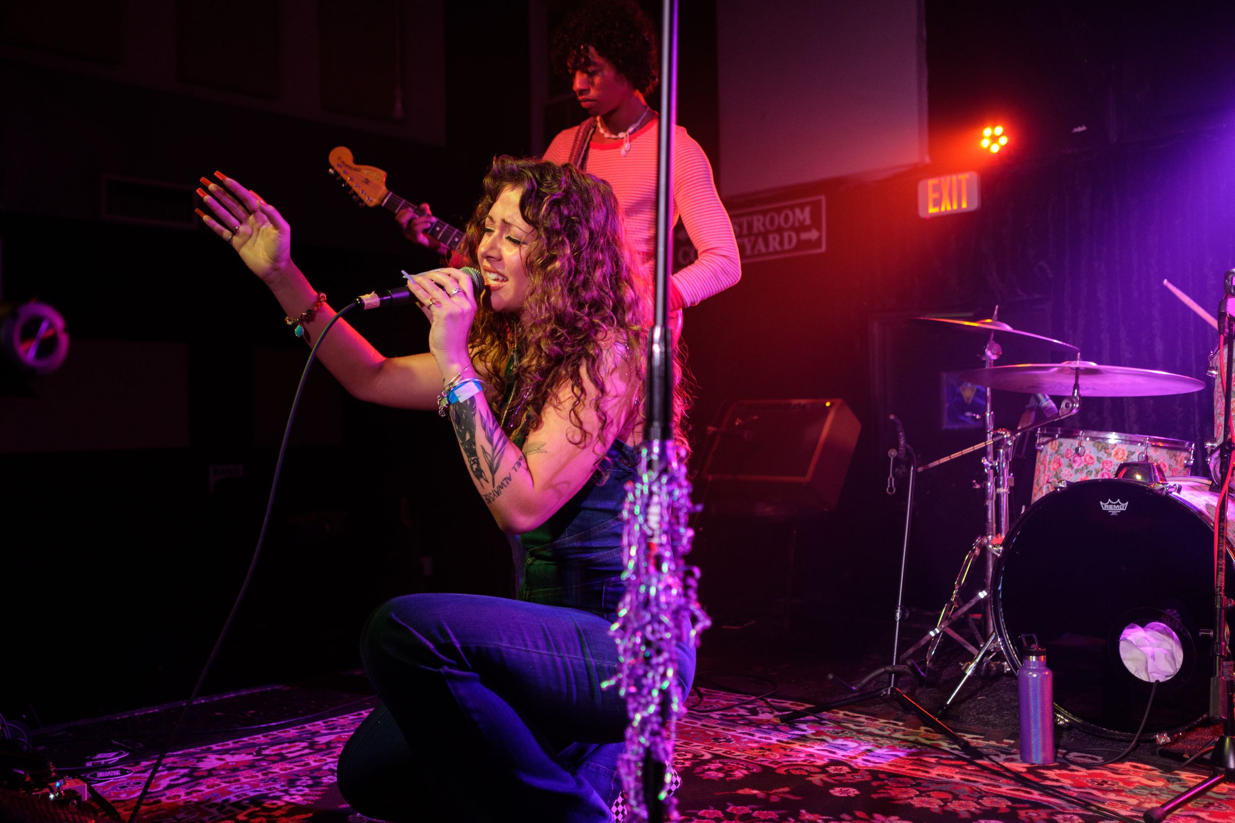 A dramatic concert moment captured under red stage lights with musicians and equipment visible.