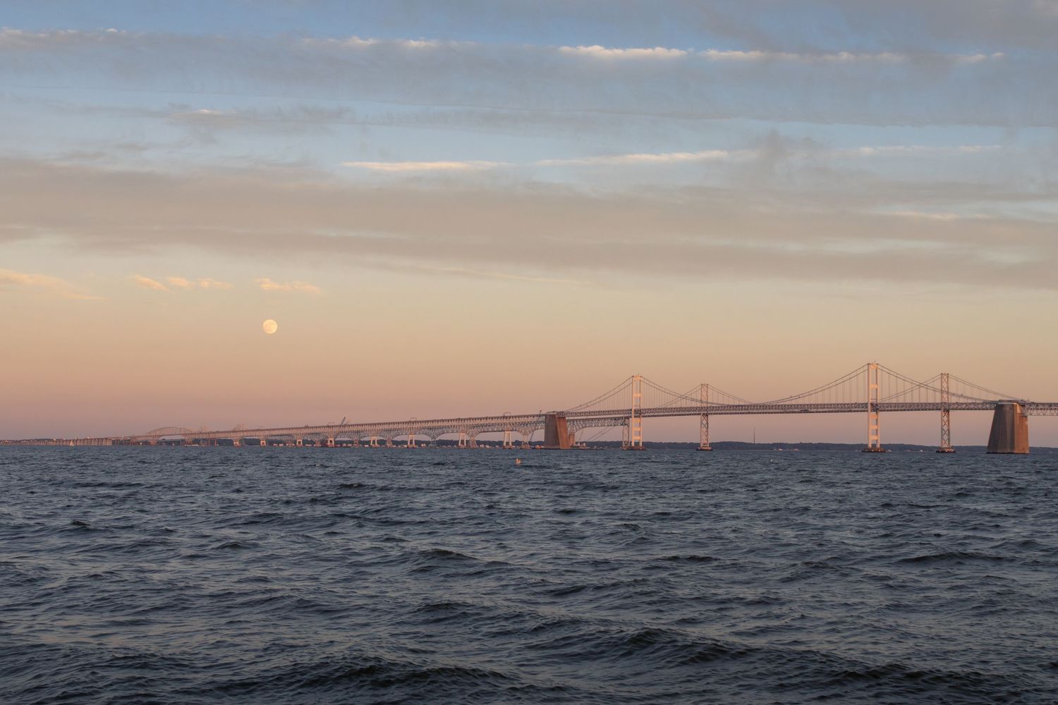 Chesapeake Bay Bridge silhouetted against a breathtaking sunset, with a radiant Strawberry Moon rising above the water