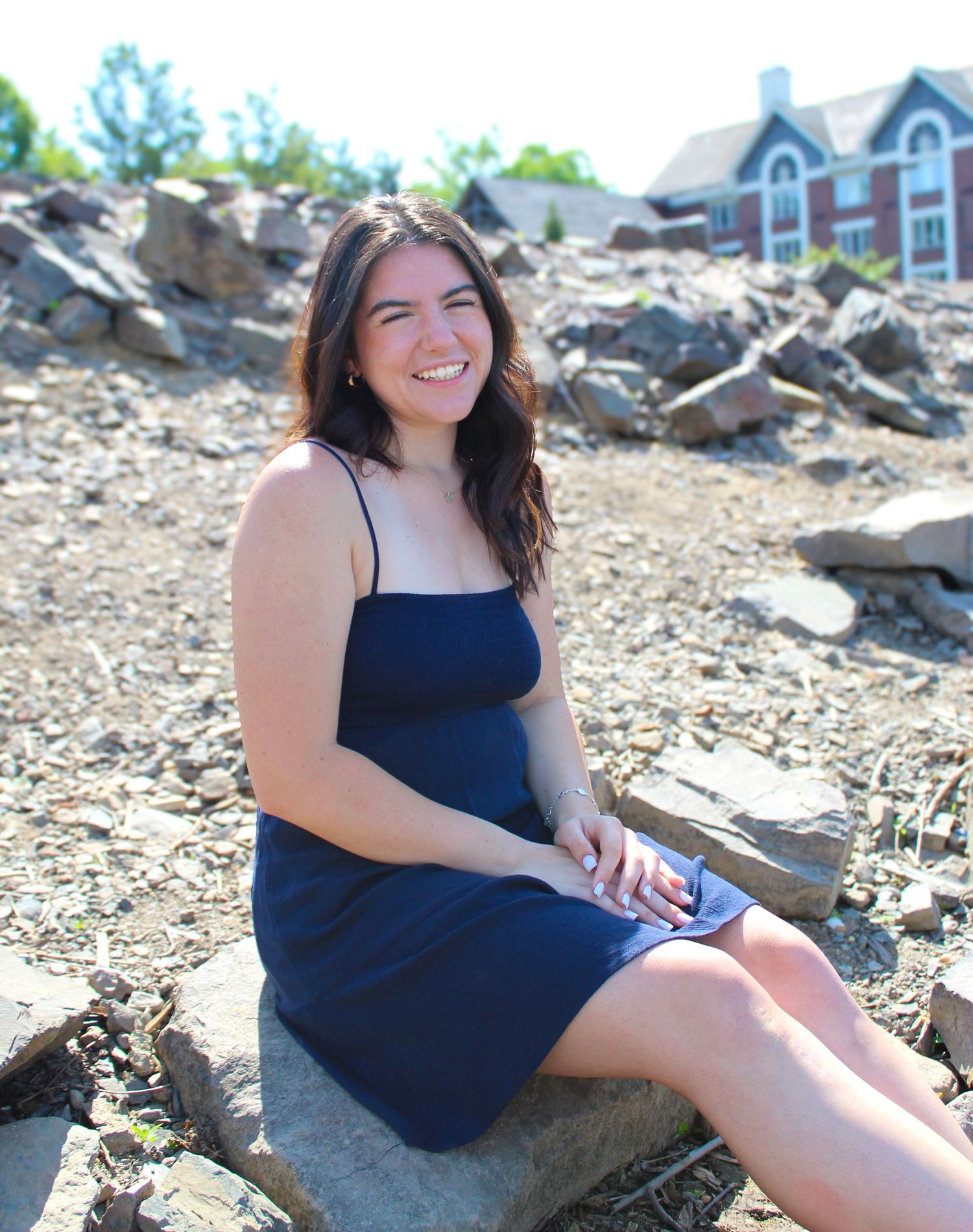 Person in navy dress sitting on rocks with houses visible in background.