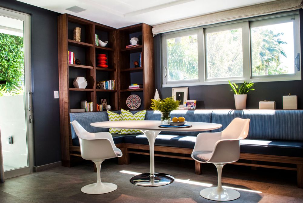 Modern dining nook features built-in bench seating, white tulip table and chairs, and dark wood built-in shelving.