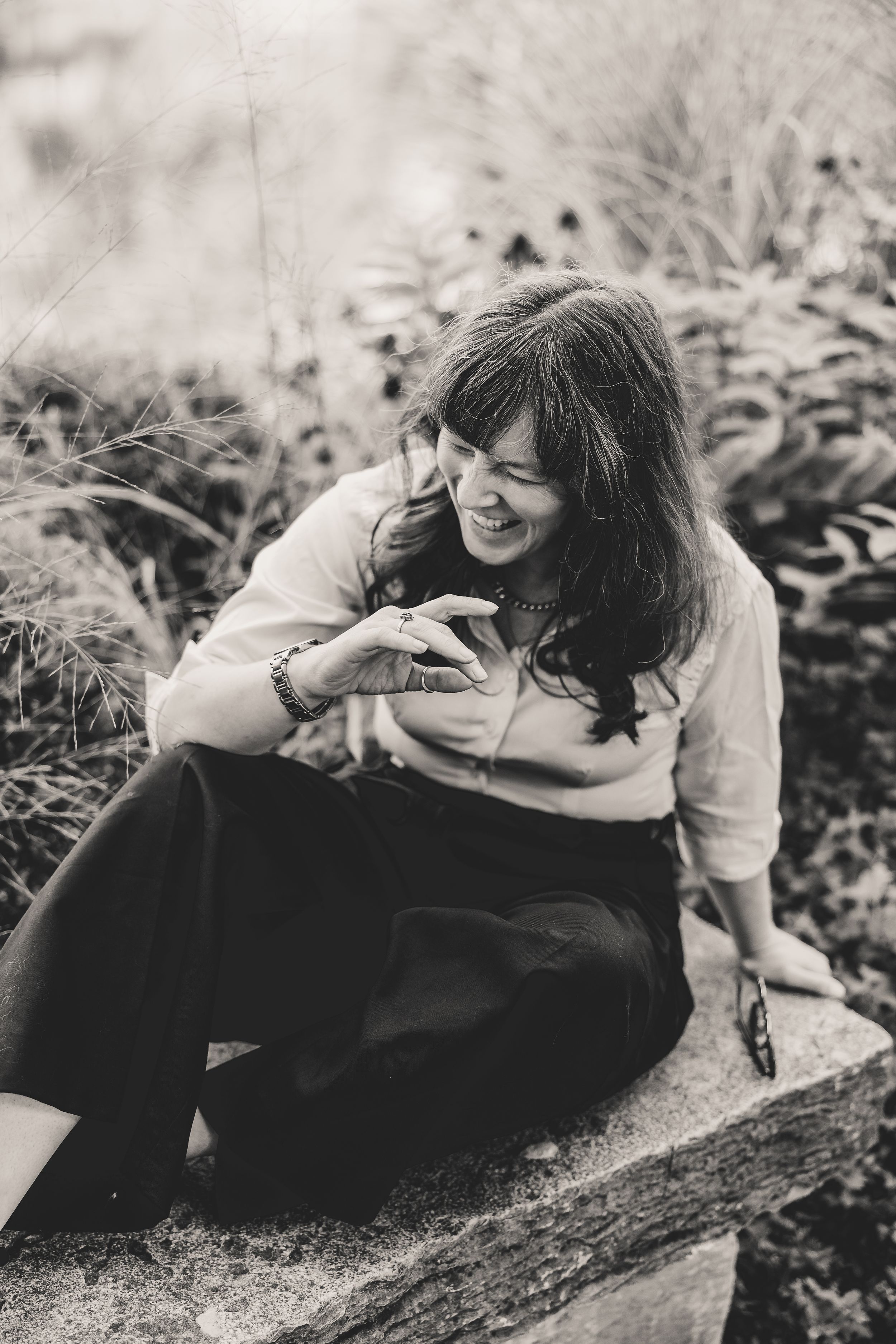 A black and white sequence of images that depict a woman laughing on a bench in a garden.