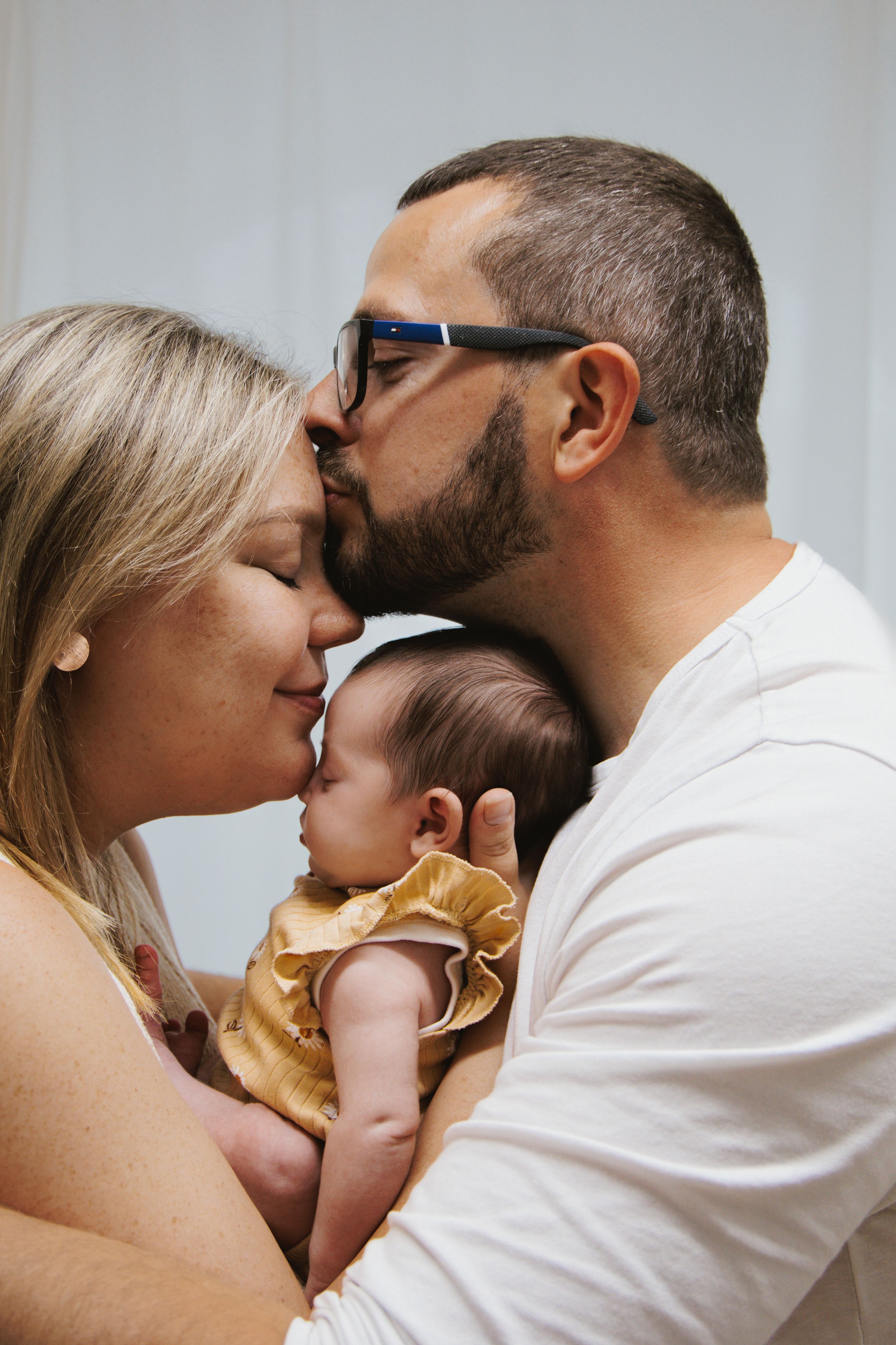 Loving parents kissing over their sleeping newborn baby dressed in gold ruffled outfit.