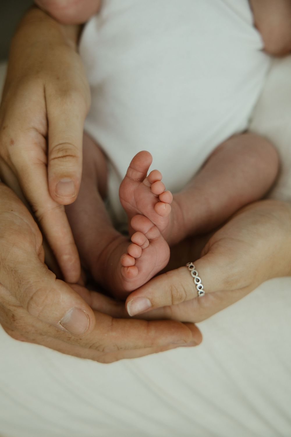 Close-up of adult hands cradling tiny newborn baby feet, with a silver ring visible on one finger.