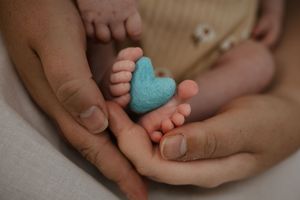 Parents cupping newborn baby feet with a small blue felt heart between them.