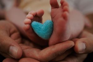Loving parents hands cradling newborn baby feet with a blue felt heart.