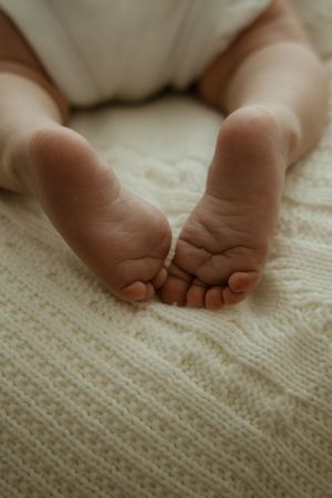 Close-up of tiny newborn baby feet resting on a soft cream knitted blanket.