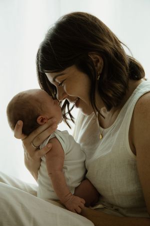 A smiling mother tenderly holds her newborn baby close, touching foreheads in a warm, intimate moment.