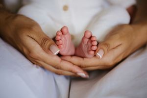 Close-up of a mother's hands gently cradling tiny newborn baby feet, symbolizing love and new life.