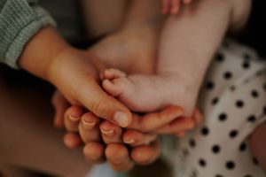 Multiple generations of hands stacked together in a tender family moment, showing connection between grandparents, parents, and baby.