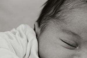Close-up black and white photo of a sleeping newborn baby's face and dark hair.