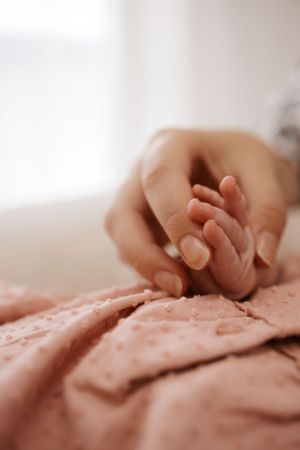 Mother's hand tenderly holding newborn baby's tiny hand on pink textured blanket.