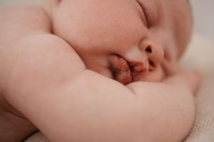 Peaceful sleeping newborn baby with chubby cheeks resting on soft cream blanket.