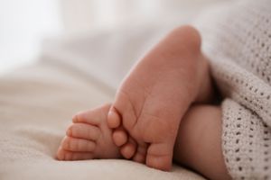 Tiny newborn baby feet peeking out from under a soft knit white blanket.