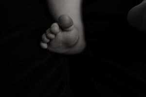 Black and white close-up of a newborn baby's tiny foot against a dark background.