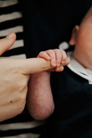 Newborn baby's tiny hand grasping an adult's finger in a close-up shot, symbolizing new life and parental bond.