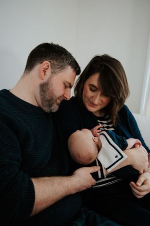 New parents lovingly gazing down at their newborn baby dressed in a sailor outfit while sitting together.