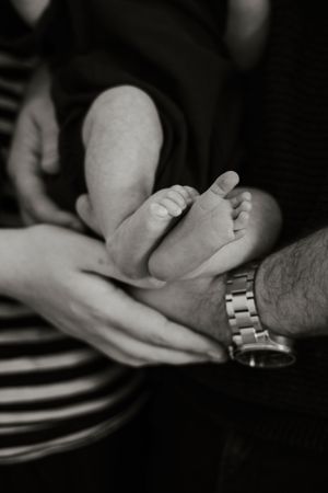 Black and white close-up of parents cradling newborn baby feet in their hands, father wearing a silver watch.
