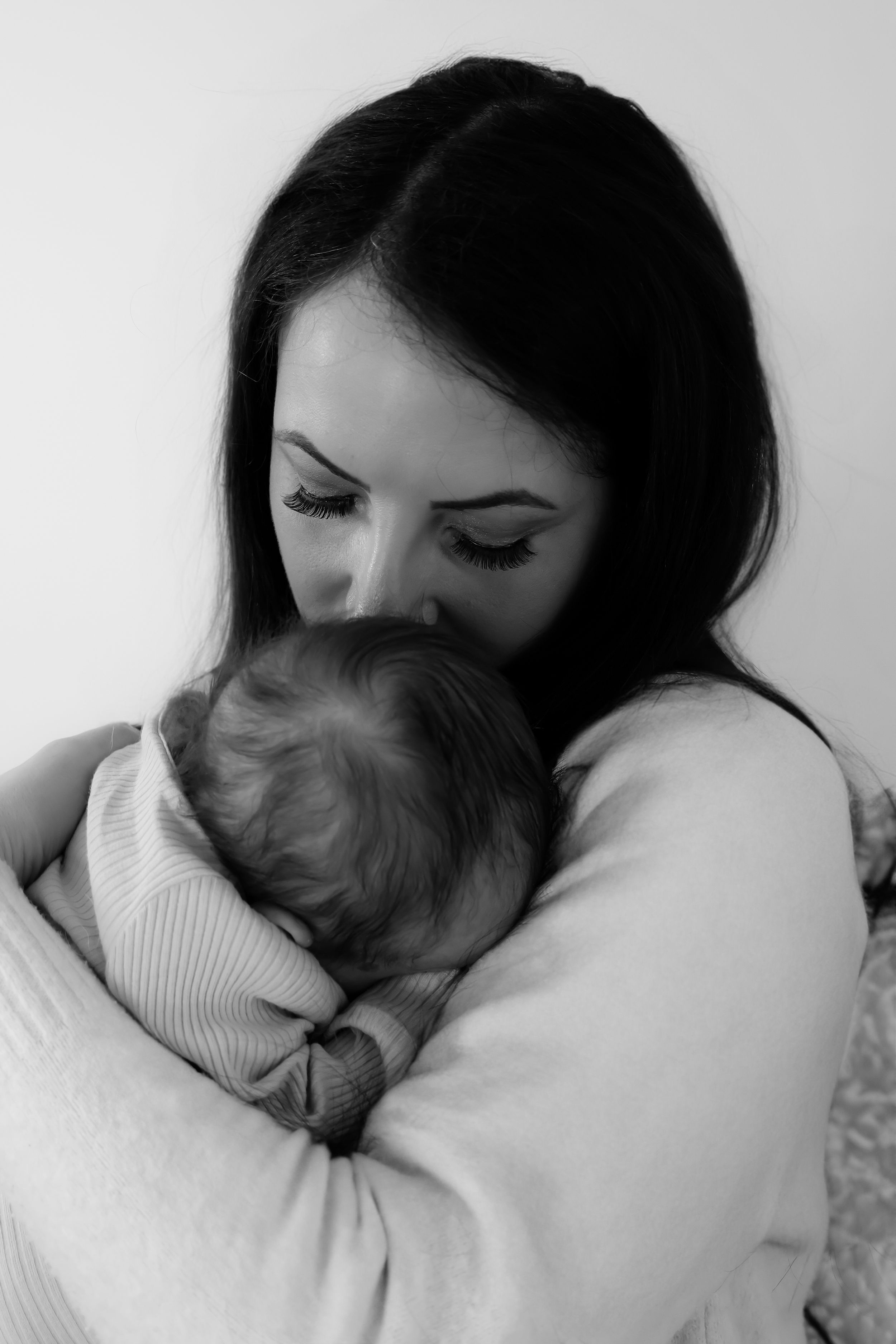 Black and white portrait of a mother tenderly holding and kissing her sleeping newborn.
