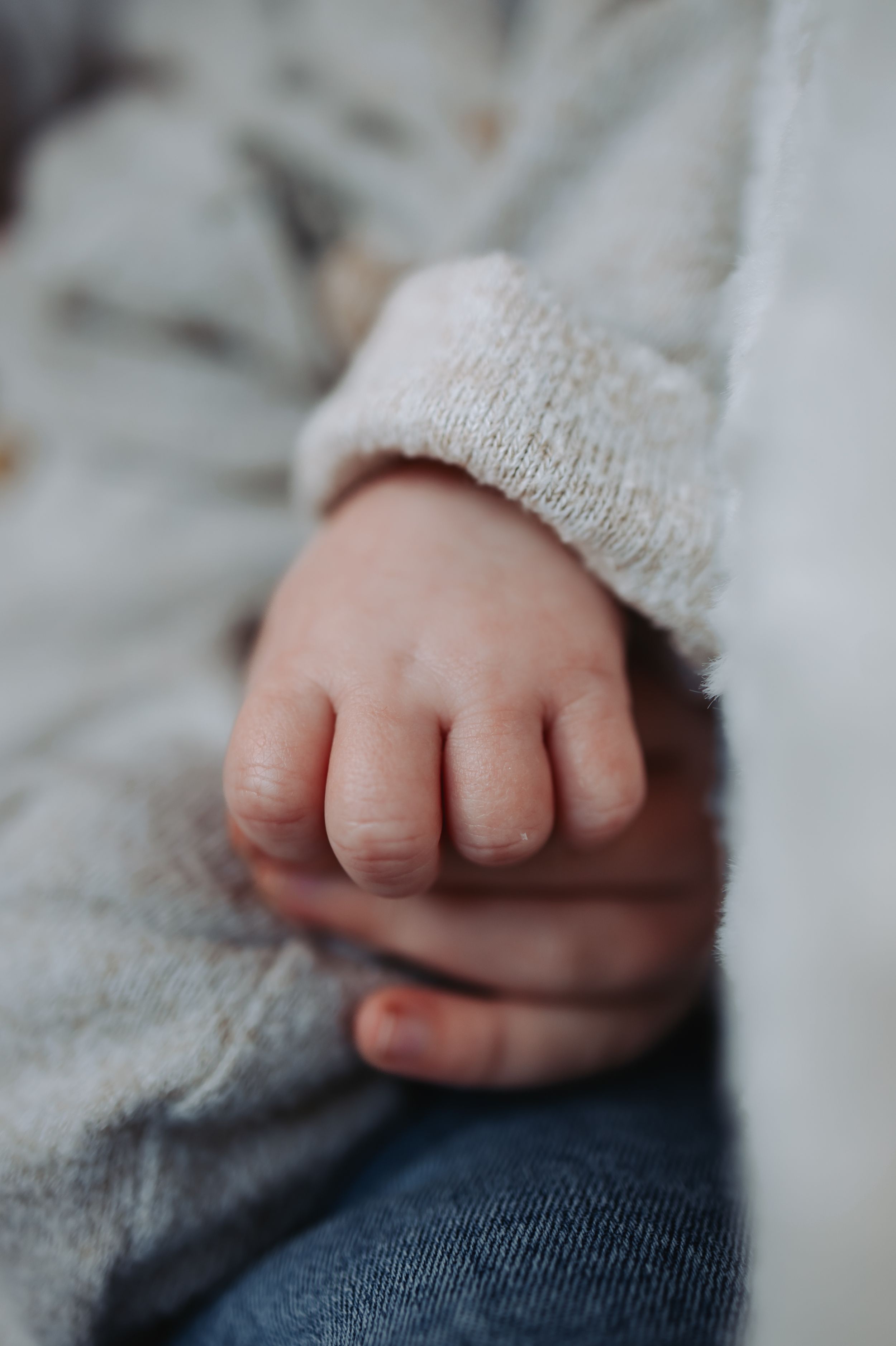 Close-up of a newborn baby's tiny hand resting on an adult's hand in a cozy knit sleeve.