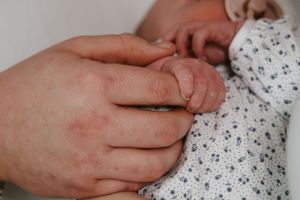 Close-up of an adult hand gently holding a newborn baby's tiny hand.