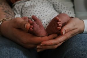 Parent's hands tenderly cradling the tiny bare feet of a newborn baby.